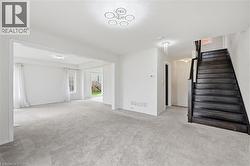 Open concept living area featuring light gray carpeting, a dark wood staircase, and recessed lighting - 