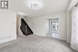 Carpeted living area featuring a dark wood staircase with balusters, a contemporary ceiling light fixture, and an arched doorway leading to a tiled entryway - 