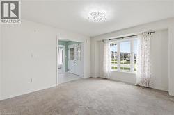 Bright room featuring a large multi-pane window, flush-mount circular lighting, light gray carpet flooring, white baseboards, and a framed entryway with double doors - 