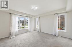 Bright interior room with multiple windows, light-colored carpet, white walls, and a decorative ceiling light fixture - 