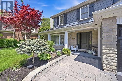 Gray siding exterior with stone accents, a covered front porch, a dark paneled entry door, and a paver walkway - 3500 Regal Road, Burlington, ON - Outdoor With Deck Patio Veranda