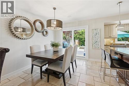 Dining area featuring light-toned rectangular floor tiles, a dark-stained wood dining table, and a linear pendant light fixture - 3500 Regal Road, Burlington, ON - Indoor Photo Showing Dining Room