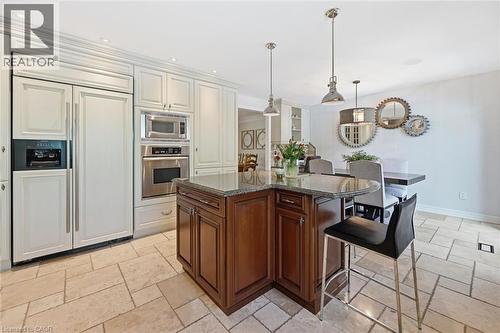 Open-concept kitchen featuring an L-shaped island with granite countertop, integrated refrigerator, built-in stainless steel microwave and oven, recessed lighting, and tile flooring - 3500 Regal Road, Burlington, ON - Indoor Photo Showing Kitchen