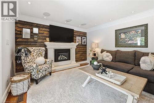 Living space featuring a prominent fireplace with a decorative mantel, wood-finish accent wall, crown molding, recessed lighting, and wood-finish flooring - 3500 Regal Road, Burlington, ON - Indoor Photo Showing Living Room With Fireplace