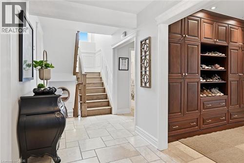 Entryway featuring extensive built-in cabinetry with paneled doors and open shelving, light-toned stone tile flooring, and a hardwood staircase with white wainscoting - 3500 Regal Road, Burlington, ON - Indoor Photo Showing Other Room