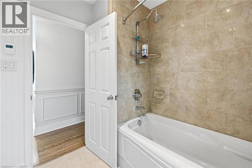 Bathtub and shower combination featuring beige natural stone-look wall tiling, a chrome shower fixture, and a white porcelain tub - 3500 Regal Road, Burlington, ON - Indoor Photo Showing Bathroom