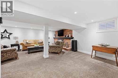 Spacious lower-level area featuring textured carpet, recessed lighting, and a brick-faced fireplace with a dark wood mantel - 3500 Regal Road, Burlington, ON - Indoor Photo Showing Living Room
