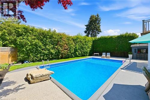 Rectangular inground pool featuring concrete surround, privacy hedging, and an outdoor bar structure - 3500 Regal Road, Burlington, ON - Outdoor With In Ground Pool With Backyard