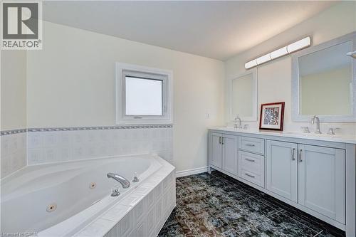 Bathroom featuring a corner jetted tub, dual vanities with light gray cabinetry, and dark patterned floor tiling - 519 Yorkshire Drive, Waterloo, ON - Indoor Photo Showing Bathroom