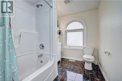Bathroom featuring a tub/shower combination with chrome fixtures, a toilet, an arched window, and dark patterned tile flooring - 519 Yorkshire Drive, Waterloo, ON - Indoor Photo Showing Bathroom