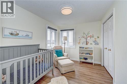 Hardwood-style flooring throughout this room featuring a ceiling-mounted light fixture, white bi-fold closet doors, and two windows with blinds - 519 Yorkshire Drive, Waterloo, ON - Indoor Photo Showing Bedroom