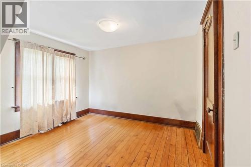 Room featuring light wood-finish flooring, a wood-trimmed window, a flush-mount ceiling light fixture, a wooden door with hardware, and white walls - 151 Louisa Street, Kitchener, ON - Indoor Photo Showing Other Room