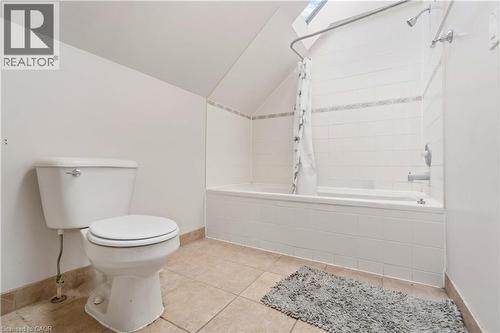 Bathroom featuring a white toilet, tiled flooring, a bathtub with shower, white subway tile surround, and a skylight - 151 Louisa Street, Kitchener, ON - Indoor Photo Showing Bathroom