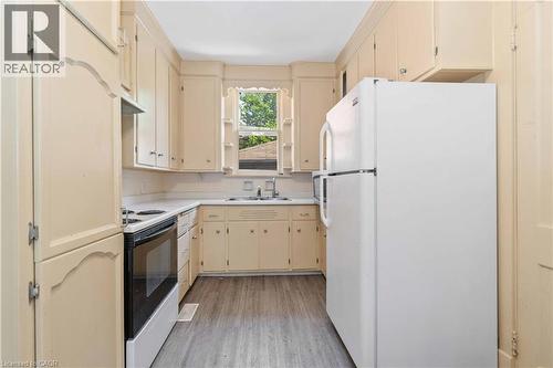 Galley kitchen featuring light-toned cabinetry, white countertops, and wood-finish flooring - 151 Louisa Street, Kitchener, ON - Indoor Photo Showing Kitchen With Double Sink