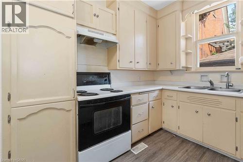 Cream-colored cabinetry with decorative accents, a black electric range with an overhead exhaust, a double basin stainless steel sink, light-toned countertops, and wood-finish flooring - 151 Louisa Street, Kitchener, ON - Indoor Photo Showing Kitchen With Double Sink
