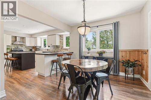 Open-concept kitchen and dining area featuring wood-finish flooring, white cabinetry, a kitchen island with seating, a stainless steel range hood, and a stone-tiled backsplash - 2207 Jester Court, Burlington, ON - Indoor Photo Showing Dining Room