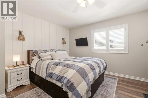 Bedroom featuring a white shiplap accent wall, wood-finish flooring, and a window with white plantation shutters - 2207 Jester Court, Burlington, ON - Indoor Photo Showing Bedroom