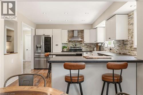 Kitchen featuring white cabinetry, stone backsplash, stainless steel appliances, dark countertops, and wood-finish flooring - 2207 Jester Court, Burlington, ON - Indoor Photo Showing Kitchen With Upgraded Kitchen
