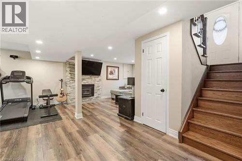 Spacious lower level featuring wood-finish flooring and a stone-clad fireplace with a hearth - 2207 Jester Court, Burlington, ON - Indoor Photo Showing Gym Room