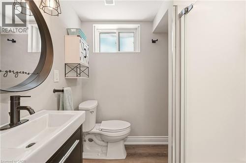 Bathroom featuring a dark wood-finish vanity with an integrated white sink, a matte black faucet, and a large circular mirror with a dark frame - 2207 Jester Court, Burlington, ON - Indoor Photo Showing Bathroom