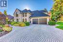 Stone facade residence featuring a circular paver driveway, two-car garage, arched windows, dark shingle roofing, and extensive landscaping - 54 Deerview Avenue, Ancaster, ON  - Outdoor With Facade 