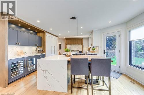 Modern kitchen featuring light wood-finish flooring, a waterfall island with a stone countertop, built-in beverage refrigerators, custom cabinetry, and recessed lighting - 54 Deerview Avenue, Ancaster, ON - Indoor