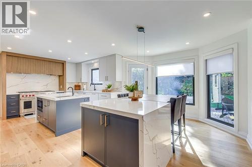 Gourmet kitchen featuring a dual-island layout with waterfall countertops, premium stainless steel appliances, light wood-finish flooring, and recessed lighting - 54 Deerview Avenue, Ancaster, ON - Indoor Photo Showing Kitchen With Upgraded Kitchen