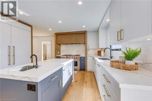 Modern kitchen featuring a central island with an integrated sink, white countertops with natural veining, and light wood-finish flooring - 54 Deerview Avenue, Ancaster, ON - Indoor Photo Showing Kitchen With Upgraded Kitchen