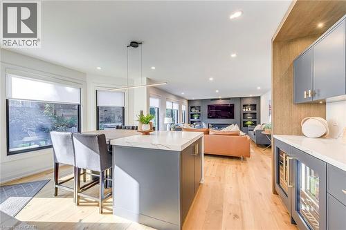 Modern kitchen island with a waterfall countertop, integrated bar seating, light wood-finish flooring, recessed lighting, and a built-in beverage cooler - 54 Deerview Avenue, Ancaster, ON - Indoor Photo Showing Kitchen With Upgraded Kitchen