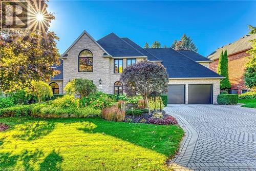 Stone veneer exterior featuring a two-car garage with dark doors, a patterned paver driveway, and a manicured front lawn with mature landscaping - 54 Deerview Avenue, Ancaster, ON - Outdoor