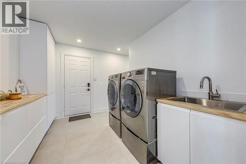 Dedicated laundry area featuring a stainless steel sink, wood-finish countertops, and white cabinetry - 54 Deerview Avenue, Ancaster, ON - Indoor Photo Showing Laundry Room