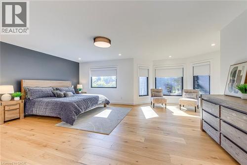 Spacious bedroom featuring light wood-finish flooring, a contemporary ceiling light fixture, recessed lighting, and a prominent accent wall - 54 Deerview Avenue, Ancaster, ON - Indoor Photo Showing Bedroom