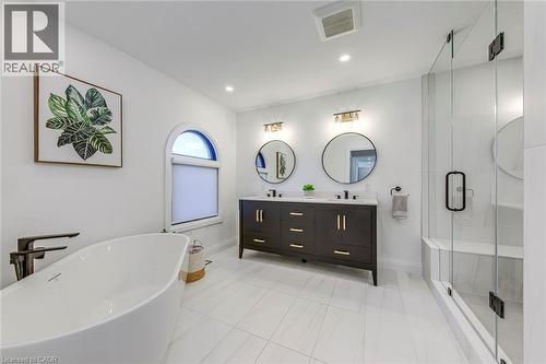 Freestanding soaking tub with dark bronze hardware, white tile flooring, and a glass-enclosed shower with integrated bench seating - 54 Deerview Avenue, Ancaster, ON - Indoor Photo Showing Bathroom