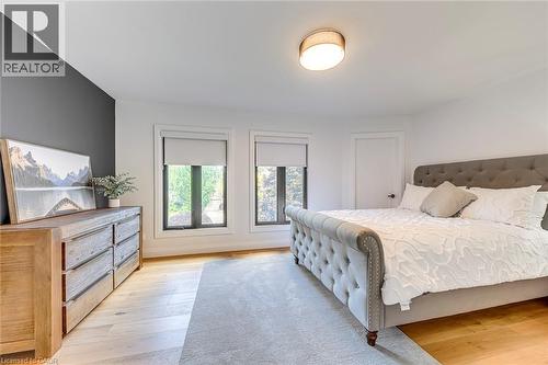 Bright room featuring two windows with roller shades, light wood-finish flooring, and a contemporary flush-mount ceiling light fixture - 54 Deerview Avenue, Ancaster, ON - Indoor Photo Showing Bedroom