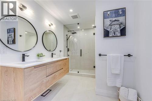 Modern bathroom featuring a floating wood-finish double vanity with integrated sinks and matte black faucets, paired with circular wall-mounted mirrors - 54 Deerview Avenue, Ancaster, ON - Indoor Photo Showing Bathroom