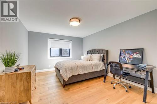 Room featuring light wood-finish flooring, a contemporary flush-mount ceiling light, and a window with a roller shade - 54 Deerview Avenue, Ancaster, ON - Indoor Photo Showing Bedroom