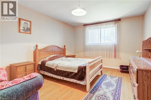 Light-filled room featuring wood-finish flooring, a ceiling-mounted light fixture, and a window with vertical blinds - 186 Adeline Avenue, Hamilton, ON - Indoor Photo Showing Bedroom
