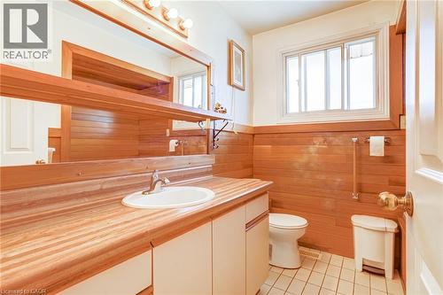 Bathroom featuring extensive wood paneling, a wood-finish vanity with an integrated sink, a large mirror with a wood frame, a window, and white square floor tiles - 186 Adeline Avenue, Hamilton, ON - Indoor Photo Showing Bathroom