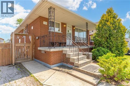 Brick facade bungalow featuring an inviting front porch with wrought iron railings and columns, concrete steps, a concrete walkway, and a wooden side gate - 186 Adeline Avenue, Hamilton, ON - Outdoor