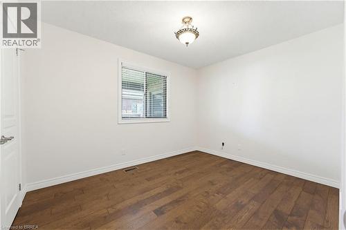 Bright interior room featuring a window with horizontal blinds, wood-finish flooring, white baseboards, and a classic-style ceiling light fixture - 6 General Street, Brantford, ON - Indoor Photo Showing Other Room