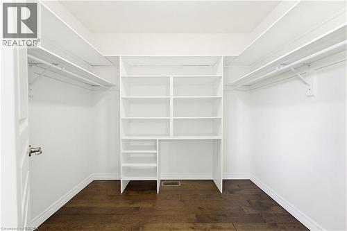 Walk-in closet featuring built-in shelving, dual hanging rods, wood-finish flooring, white baseboards, and a white interior door - 6 General Street, Brantford, ON - Indoor With Storage