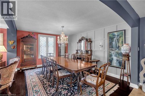 Formal dining space featuring dark wood-finish flooring, a crystal chandelier, decorative wall paneling, and a window with diamond-patterned mullions - 69 Hunter Way, Brantford, ON - Indoor Photo Showing Dining Room