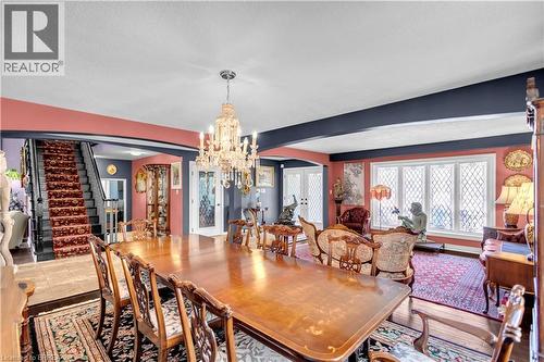 Formal dining area featuring a crystal chandelier, patterned area rugs, a large multi-pane window with diamond grilles, and a staircase with a patterned runner - 69 Hunter Way, Brantford, ON - Indoor Photo Showing Dining Room