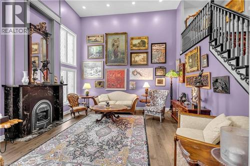 Double-height living space featuring a dark stone fireplace with decorative mantel, wood-finish flooring, a grand staircase with dark railings, and ample natural light from tall windows - 69 Hunter Way, Brantford, ON - Indoor