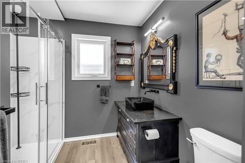 Modern bathroom with a glass-enclosed shower featuring white-and-gray patterned wall panels, a dark vanity with a rectangular vessel sink, a coordinating wall-mounted faucet, and wood-finish flooring - 69 Hunter Way, Brantford, ON - Indoor Photo Showing Bathroom