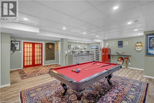 Recreation space featuring wood-finish flooring, a drop ceiling with recessed lighting, red French doors, and a built-in wet bar with cabinetry - 69 Hunter Way, Brantford, ON - Indoor Photo Showing Other Room