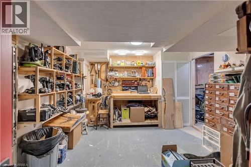 Dedicated workspace featuring extensive built-in wooden shelving, a large workbench with integrated storage, and multiple overhead lighting fixtures - 69 Hunter Way, Brantford, ON - Indoor