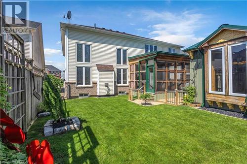 Rear exterior featuring beige siding with stone-finish foundation, a screened-in porch with green trim, and a detached structure with wood siding and large windows - 69 Hunter Way, Brantford, ON - Outdoor