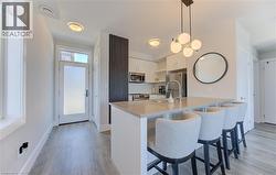 Contemporary kitchen featuring an island with ample seating, stainless steel appliances, white cabinetry, and wood-finish flooring - 