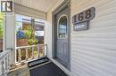 Front entry featuring a gray paneled door with an arched glass insert, white horizontal siding, and a covered porch with white turned balusters - 168 Britannia Avenue, Hamilton, ON  - Outdoor With Exterior 